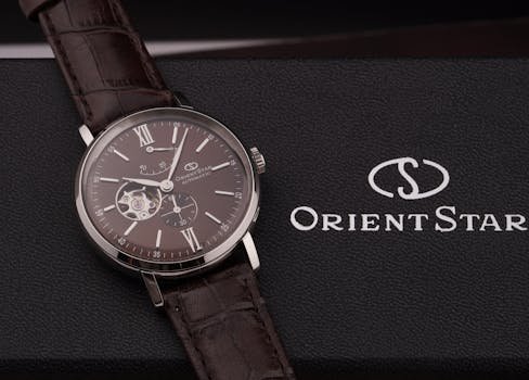 Close-up of an elegant Orient Star wristwatch with a brown leather strap on a textured box.